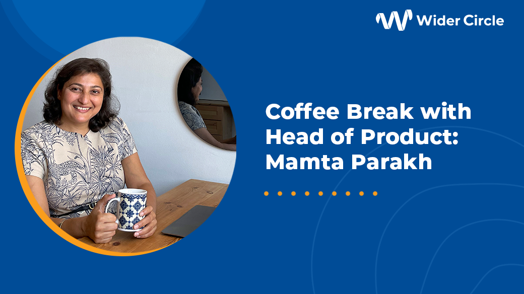 Foto de Mamta Parakh, Jefa de Producto, Wider Circle, sosteniendo una taza de café y sentada en su escritorio