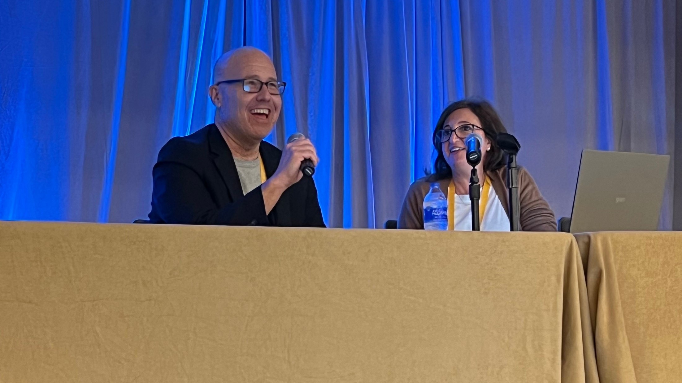 Bill Friedman and Ana Handshuh speaking together at a table with microphones at the RISE HEDIS 2022 conference